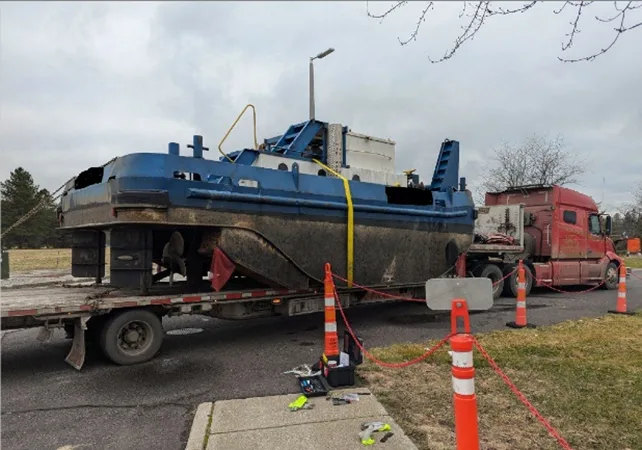 One of the intercepted tugboats loaded onto a flatbed truck. The tug is blue and white and the semi truck cab is red.